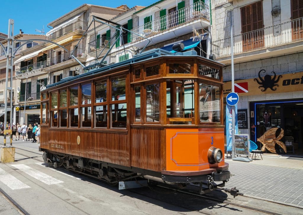 A classic wooden tram navigating the charming streets of Sóller, Mallorca under a clear blue sky.
