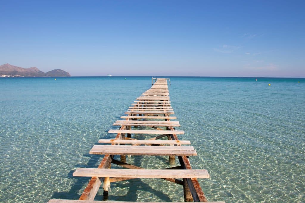 Serene wooden pier stretching into clear turquoise waters in Mallorca, Spain, under a bright blue sky.